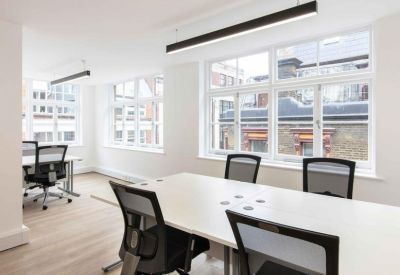Spacious office area with white desks, black chairs, and large windows.