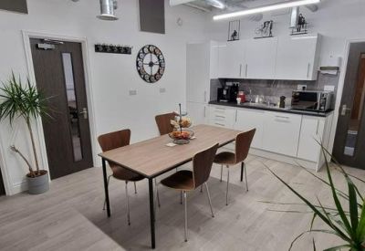 Communal kitchen area and dining table with wood flooring and potted plants.