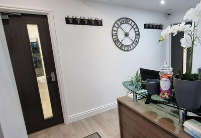 Professional reception desk with wall clock, coat hooks, and decorative flowers.