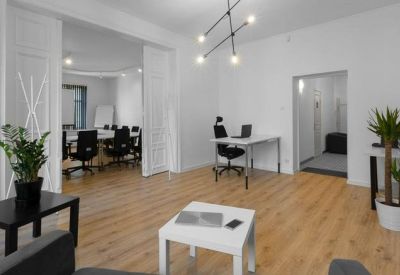 Bright open-plan lounge and coworking space with a modern chandelier and wooden floors.