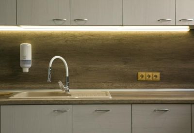 Modern communal kitchen area with wood-grain backsplash, white faucet, and grey cabinetry.