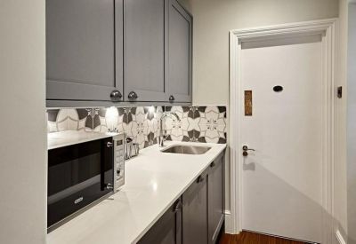 Modern kitchenette with grey cabinetry, patterned backsplash, and integrated microwave.