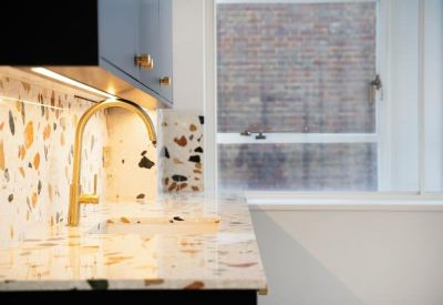 Close-up of a kitchen sink featuring a gold faucet and vibrant terrazzo backsplash.