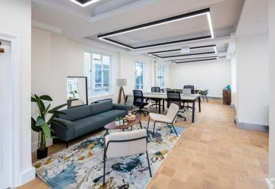 Stylish breakout lounge with a teal sofa and colorful rug adjacent to workstations.