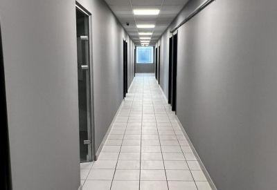 Long grey office corridor with tiled flooring and recessed ceiling lights.