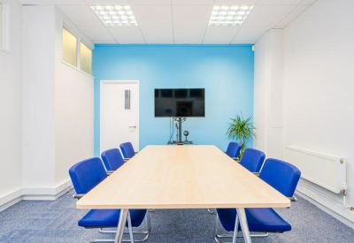 Professional meeting room featuring a light wood table, blue chairs, and a wall-mounted screen.
