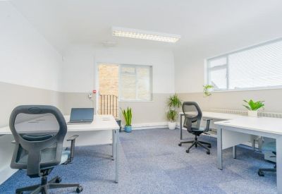 Bright private office suite with two desks and view of adjacent brick building.