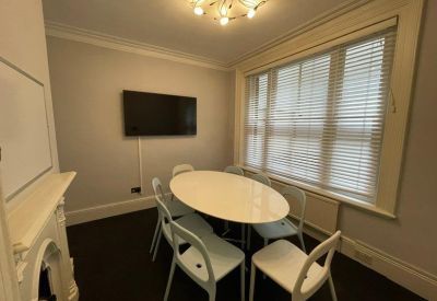 Meeting room with an oval white table, modern chairs, and a wall-mounted TV.