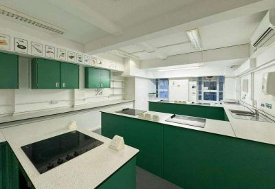 Modern teaching kitchen with green cabinetry, white countertops, and integrated electric hobs.