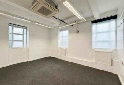 Minimalist office suite with grey carpet, dual windows, and ceiling-mounted air conditioning.