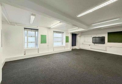 Spacious open-plan office with grey carpeting, large windows, and wall-mounted screens.