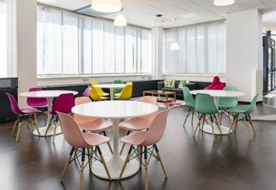 Communal breakout area with vibrant pink, yellow, and green Eames-style chairs.