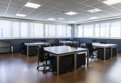 Bright open-plan workspace with multiple minimalist black desks and office chairs.