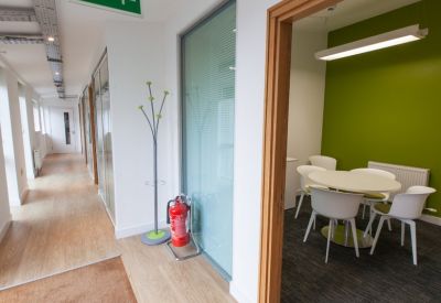 Bright breakout room with a green feature wall, round table, and a long hallway with wood-style flooring.