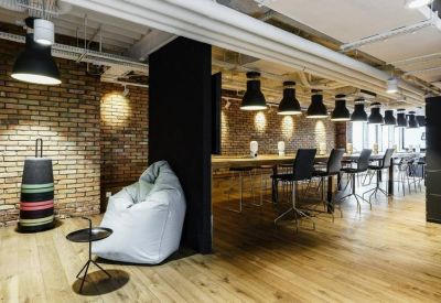 Open-plan office with long desks, bean bag chair, and exposed brick walls.