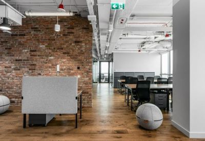 Bright open-plan office with wooden flooring, brick accent walls, and ergonomic workstations.