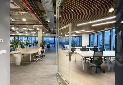 Glazed entrance to a bright office area showing desk clusters and greenery.