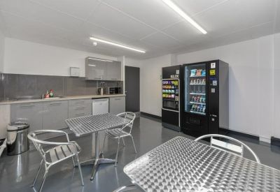 Communal break room with vending machines, kitchen units, and metal dining tables.