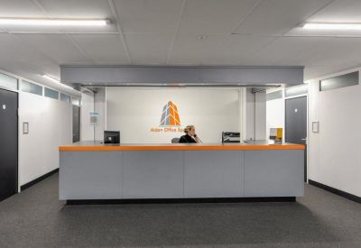 Professional reception desk with orange accents and a corporate logo on the back wall.