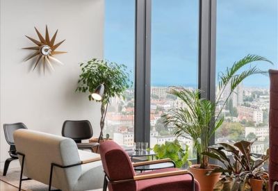 Bright lounge area with mid-century modern furniture, indoor plants, and floor-to-ceiling city views.