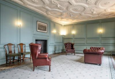 Grand lounge with ornate plaster ceiling, blue wood paneling, and leather wingback chairs.