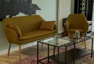 Lounge area with a yellow velvet sofa, armchair, and glass coffee tables over a patterned rug.