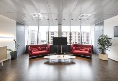 Lounge area with vibrant red sofas, a low oval coffee table, and potted plants.