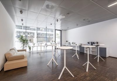 Breakout space with white high-top bistro tables and a tan leather sofa.