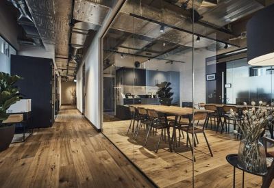 Modern coworking lounge with long wooden tables and glass partitions.