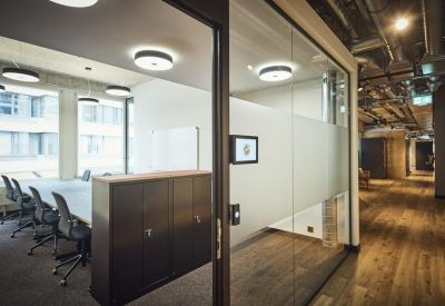 Bright glass-walled meeting room with a dark wood cabinet and black chairs.