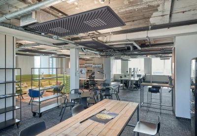 Spacious coworking area with industrial ceilings, wooden tables, and lounge seating.