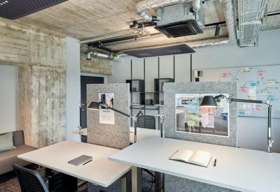 Shared workspace with desks, grey partitions, and exposed concrete walls.