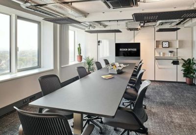 Bright conference room with a long grey table and a wall-mounted monitor.
