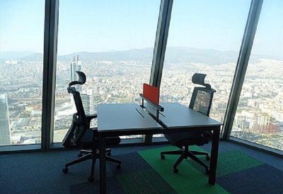 Shared office desk with ergonomic chairs overlooking a panoramic cityscape.