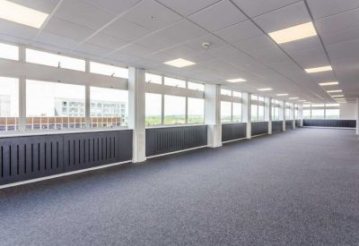 Spacious open-plan office area with large windows and grey carpeting.