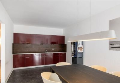 Modern office kitchen with sleek burgundy cabinetry and an adjacent dining table.
