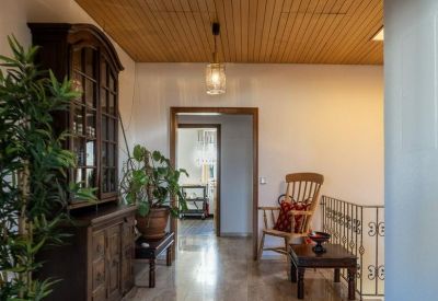 Hallway area with an ornate wooden cabinet, a rocking chair, and a large potted plant.