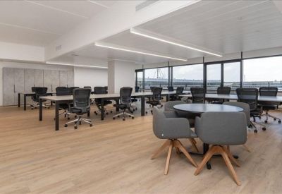 Open-plan office space featuring long white desks and views through large windows.