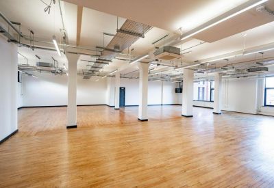 Spacious open-plan workspace with polished wooden floors and industrial ceiling pipes.