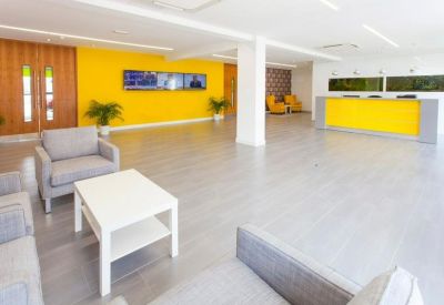 Bright reception area featuring a yellow feature wall and desk, lounge seating, and wall-mounted screens.