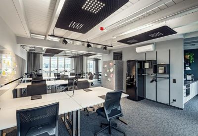 Open-plan office with white desks, ergonomic black chairs, and a small kitchen area.