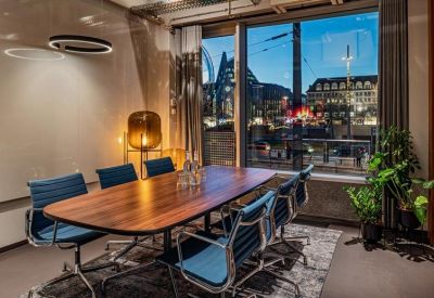 Professional meeting room with a dark wood table, blue chairs, and a large window at dusk.