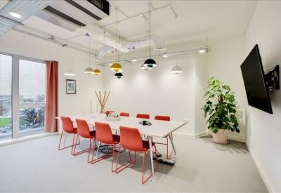 Bright meeting room with a long white table, red chairs, and designer pendant lights.