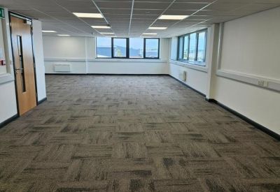 Spacious open-plan office with grey carpet tiles, white walls, and a timber-finish entrance door.