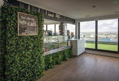 Bright café area with a green plant wall and city views through large windows.