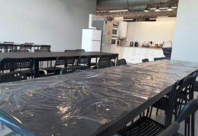 Spacious communal dining area with long tables and a modern kitchen in the background.