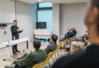 Presentation taking place in a bright meeting room with a whiteboard and seated audience.