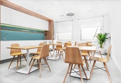 Bright communal kitchen and dining area with wooden chairs and a teal backsplash.