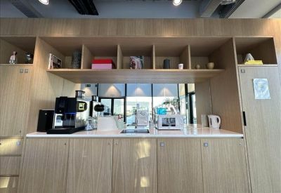 Modern office kitchen area with light wood cabinetry and a white countertop.