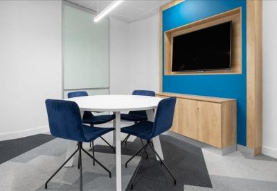 Small breakout room with round white table, blue chairs, and wall-mounted TV.